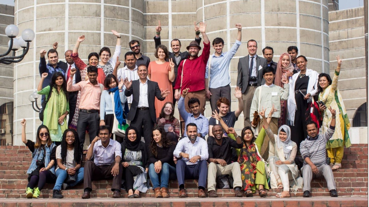 A large group of people, sitting and standing, smiling and laughing to camera with their arms waving in the air.